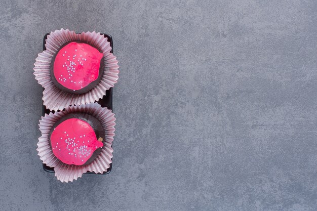 Boules de chocolat avec glaçage rose sur plaque sombre.