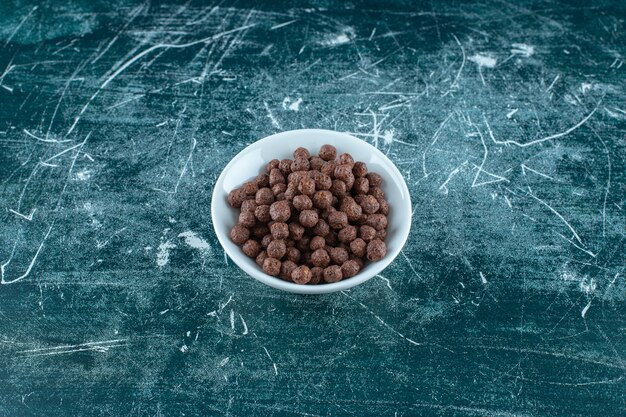 Boules de maïs au chocolat dans un bol, sur fond bleu. photo de haute qualité