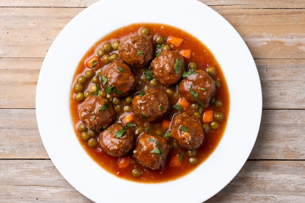 Photo gratuite des boulettes de viande, des pois verts et des carottes avec de la sauce tomate sur une table en bois.