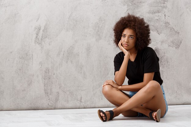 Bouleversé la belle fille africaine assise sur le mur lumineux.