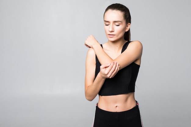 Bouleversé la brune jeune femme blessée au bras pendant l'entraînement sportif, touche son poignet isolé sur mur blanc