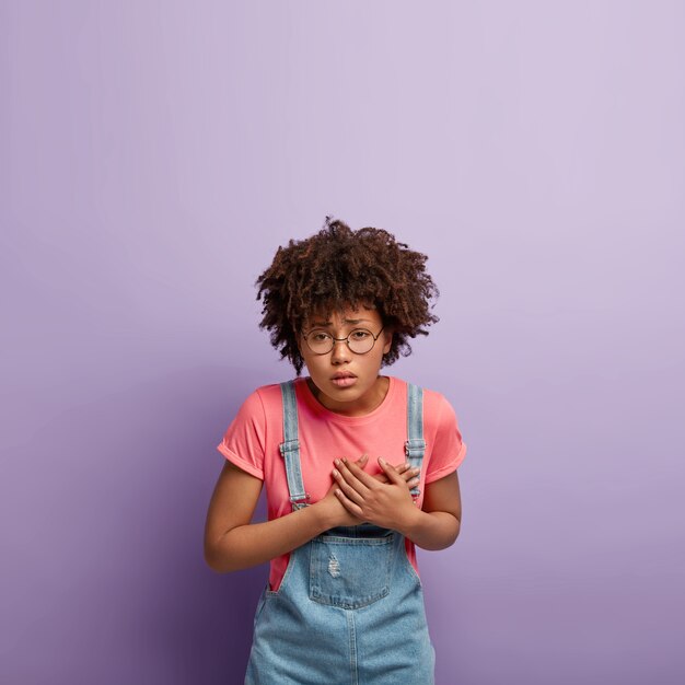 Bouleversé déprimé jeune femme avec un afro posant en salopette