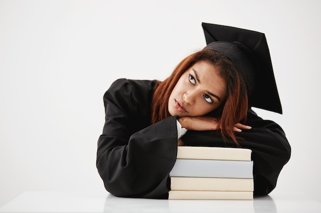 Bouleversé diplômé africain couché sur des livres pensant assis. Copiez l'espace.