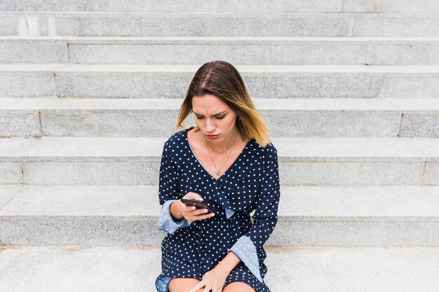 Bouleversé femme assise sur l&#39;escalier en regardant smartphone