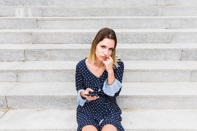 Photo gratuite bouleversé la femme assise sur l'escalier en tenant le téléphone portable