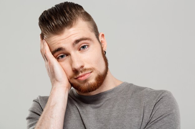 Bouleversé le jeune bel homme posant sur le mur gris.