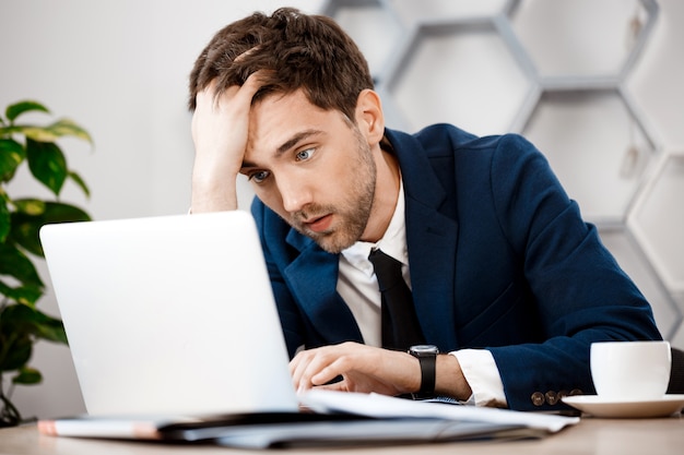 Bouleversé le jeune homme d'affaires assis à l'ordinateur portable, fond de bureau.