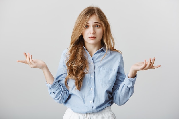 Bouleversé par le manque de choix. Portrait de modèle féminin de race blanche misérable sombre étalant les paumes et soulevant les sourcils, se sentant désespéré et confusion, n'ayant aucune idée de ce qu'il faut faire, debout sur un mur gris