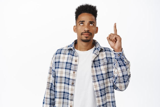 Photo gratuite bouleversé les sourcils de sillon de gars afro-américain pointant et levant les yeux avec une expression de visage triste déçu sceptique quant au texte promotionnel debout sur fond blanc