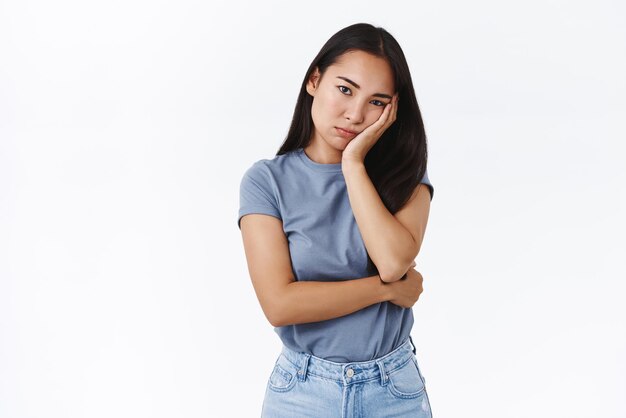 Bouleversée ennuyée ou troublée jeune fille asiatique debout affligée ou triste penchée sur la paume regarde avec apathie et ennui caméra debout agacé ne veut pas entendre parler sans intérêt fond blanc