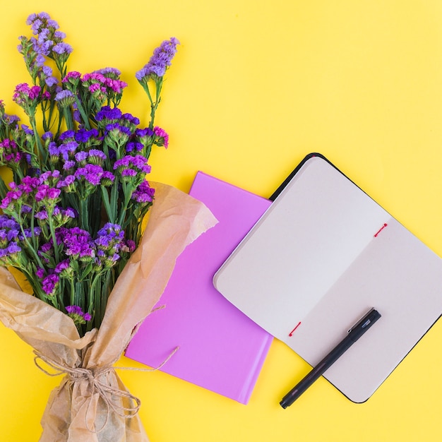 Photo gratuite bouquet de fleurs; agendas et stylo sur fond jaune