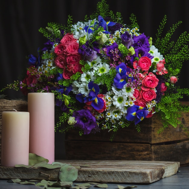 Bouquet de fleurs et bougies roses sur un espace en bois rustique.