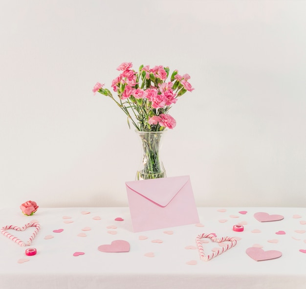 Photo gratuite bouquet de fleurs dans un vase près d'un ensemble de coeurs en papier, d'une enveloppe et de cannes de bonbon