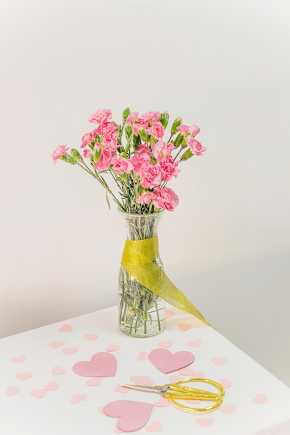 Bouquet de fleurs dans un vase avec ruban près de ciseaux et coeurs de papier