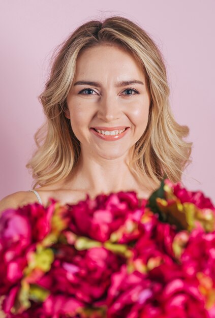 Bouquet de fleurs défocalisé devant une jeune femme souriante sur fond rose