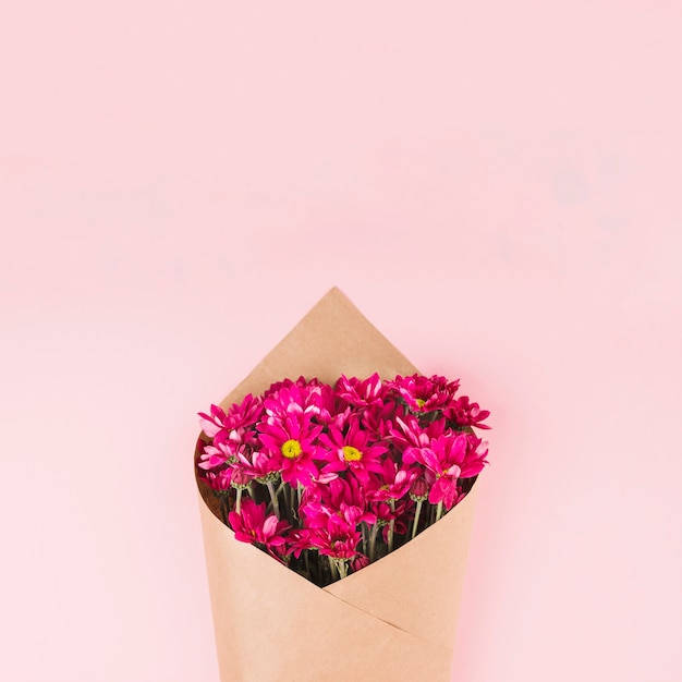 Bouquet de fleurs enveloppé de papier brun sur fond rose