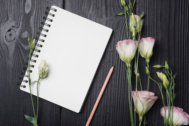 Bouquet de fleurs d&#39;eustoma violet avec un crayon et un bloc-notes à spirale blanche sur un bureau en bois