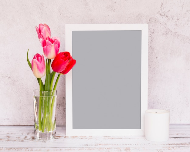 Bouquet de fleurs fraîches sur les tiges dans un vase près du cadre et de la bougie