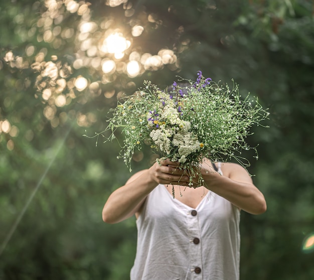 Un bouquet de fleurs sauvages dans les mains d'une fille sur un arrière-plan flou dans la forêt.