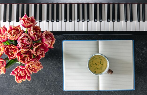 Bouquet de fleurs de tulipes pour piano, tasse de thé et bloc-notes sur un fond sombre