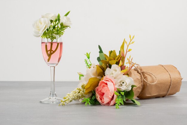 Bouquet de fleurs et un verre de vin rosé sur surface grise.