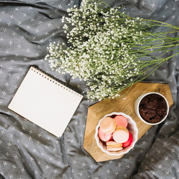 Bouquet près de bloc-notes et desserts sur le lit