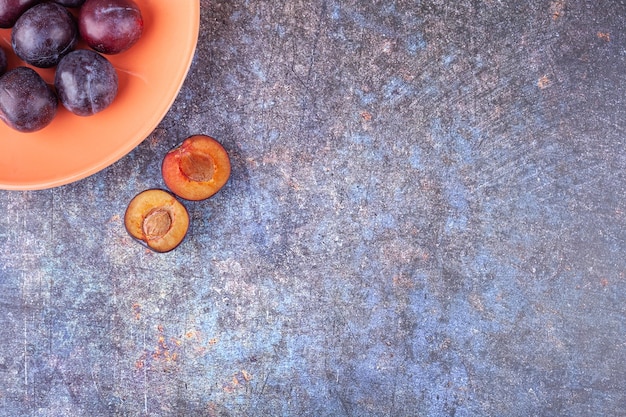 Bouquet de prunes violettes fraîches placées sur une assiette orange.