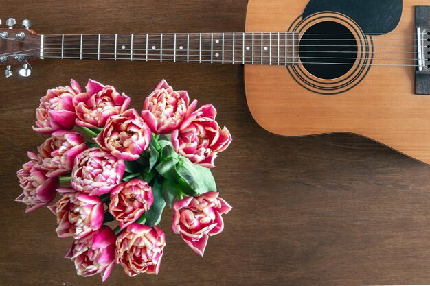 Bouquet de tulipes roses et de guitare acoustique sur un fond en bois vue du haut