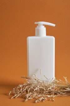 Bouteille blanche avec distributeur sans logo sur fond marron, herbe sèche, concept de cosmétiques naturels