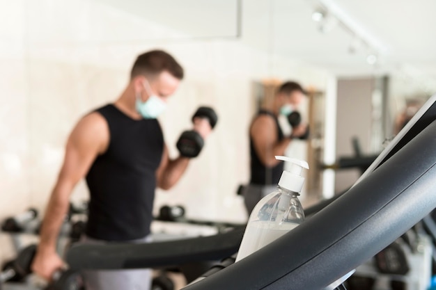 Bouteille de désinfectant pour les mains reposant sur un équipement de gym avec homme défocalisé travaillant