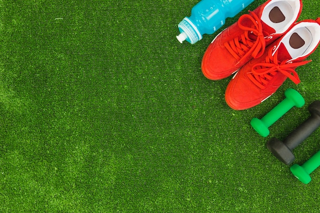 Bouteille d&#39;eau; chaussures de sport rouges et haltères sur gazon vert