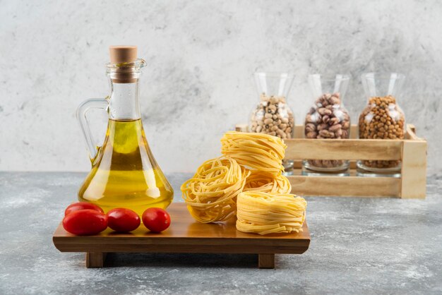 Une bouteille d'huile avec des pâtes au nid crues et des tomates cerises.