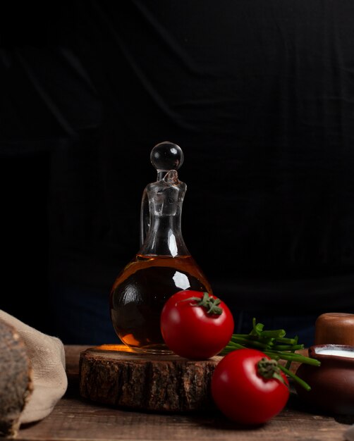 Bouteille d'huile, tomates et herbes sur le morceau de bois