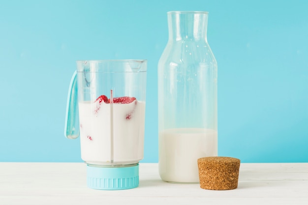 Bouteille et mélangeur avec du lait et des fraises sur le dessus de table