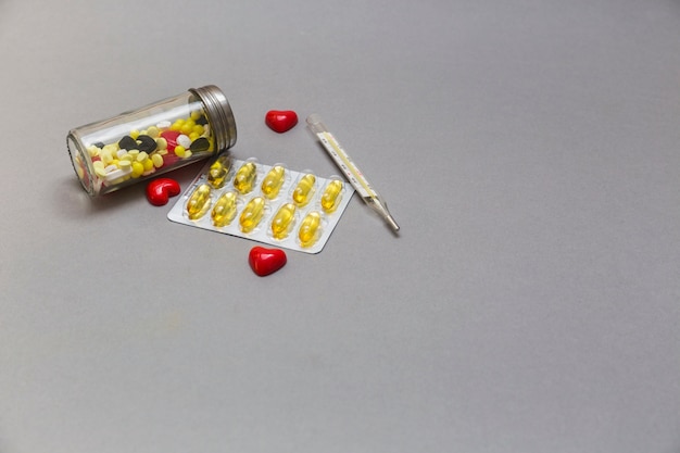 Bouteille de pilules; coeur rouge et thermomètre sur fond gris