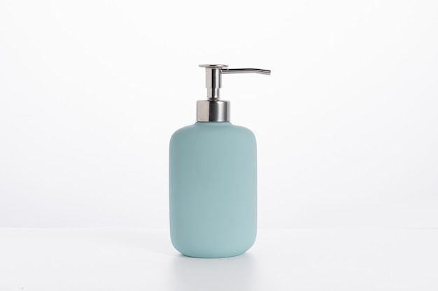Bouteille de savon en verre bleu isolé sur un mur blanc