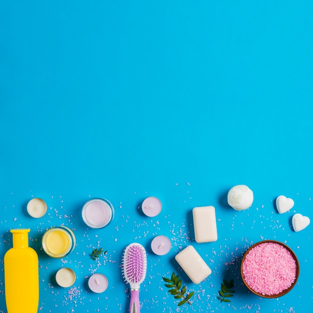 Photo gratuite bouteille de shampoing; crème; savon; bombe de bain avec du sel rose sur fond bleu