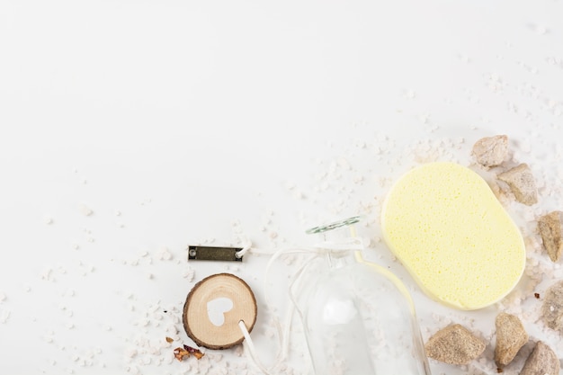 Bouteille en verre avec un couvercle ouvert; éponge; pierres de spa sur le sel sur fond blanc