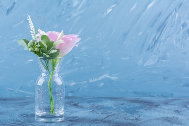 Bouteille en verre de fleur rose simple avec des feuilles sur bleu.