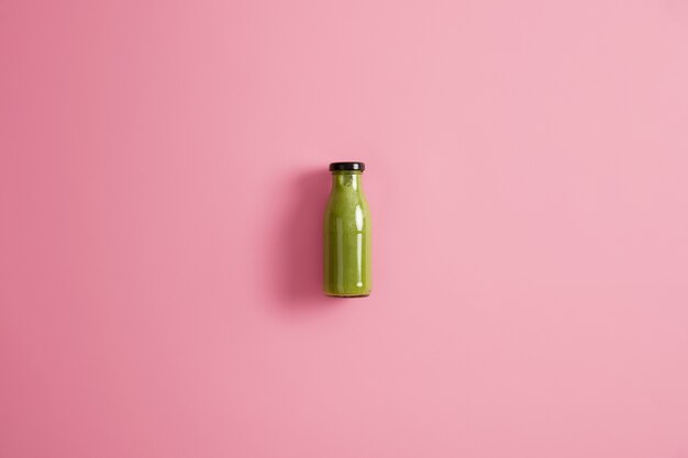 Bouteille en verre de smoothie rafraîchissant à base d'épinards, de concombre et d'avocat, faible en calories, isolé sur fond rose. Concept de régime et de mode de vie sain. Mélange de légumes verts à boire