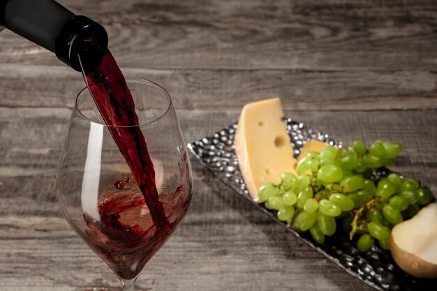 Une bouteille et un verre de vin rouge avec des fruits sur bois