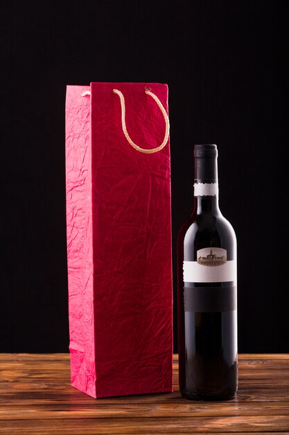 Bouteille de vin et sac en papier rouge sur une table en bois sur fond noir