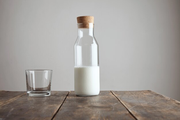 Bouteille vintage en liège fermé avec du lait sur une table en bois âgée près de verre transparent whisky rox, isolé sur blanc. Beaux reflets