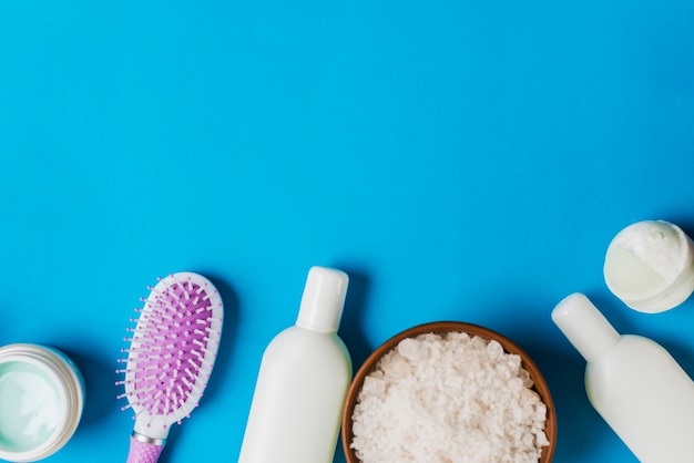 Bouteilles de cosmétiques; crème; brosse à cheveux et sel sur fond bleu