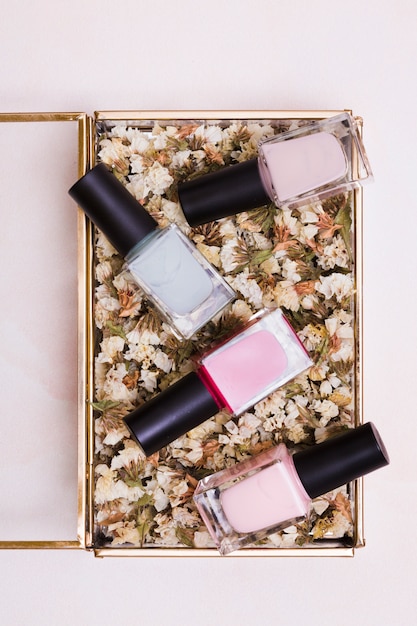 Photo gratuite bouteilles de vernis à ongles roses et gris sur une boîte de limonium blanc séché sur un fond coloré