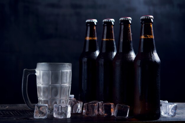 Bouteilles en verre de bière avec verre et glace sur fond sombre