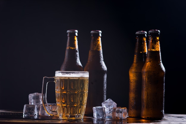 Bouteilles en verre de bière avec verre et glace sur fond sombre