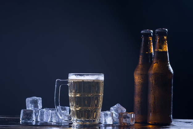 Bouteilles en verre de bière avec verre et glace sur fond sombre