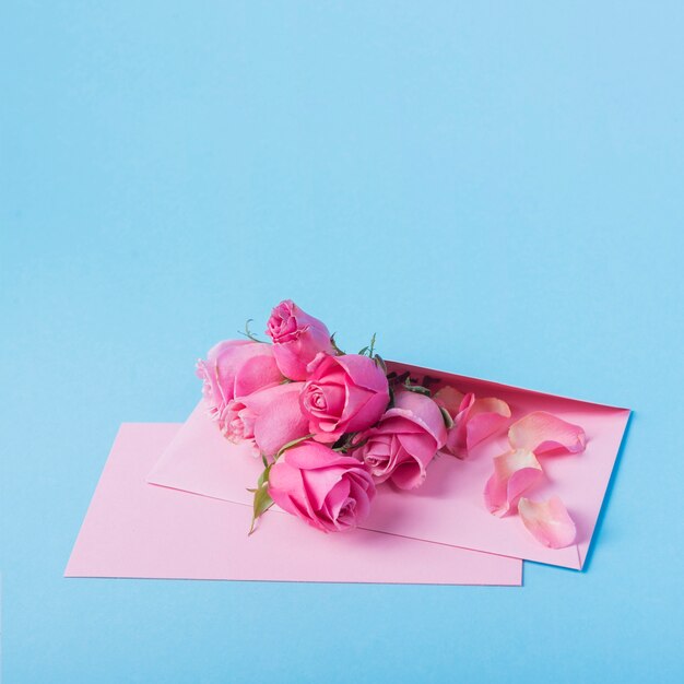 Boutons de roses avec enveloppe sur table bleue