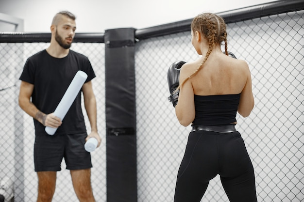 Boxe femme. Débutant dans une salle de sport. Dame dans un vêtement de sport noir. Femme avec entraîneur.